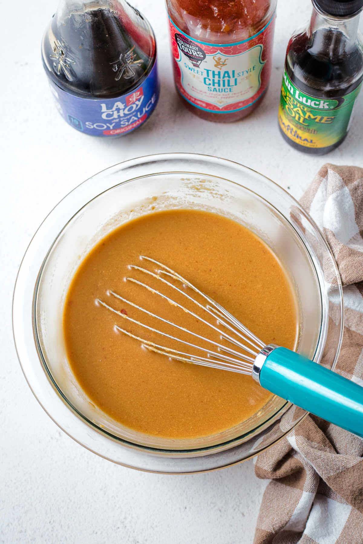 whisking together ingredients for peanut butter sauce in a glass bowl.