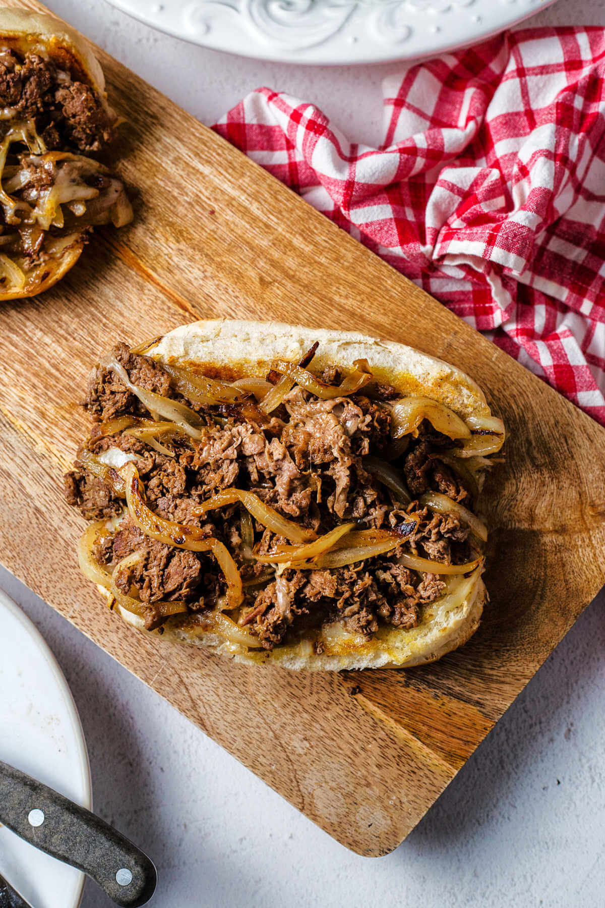 an open-face philly cheesesteak sandwich on a wooden board on a table.
