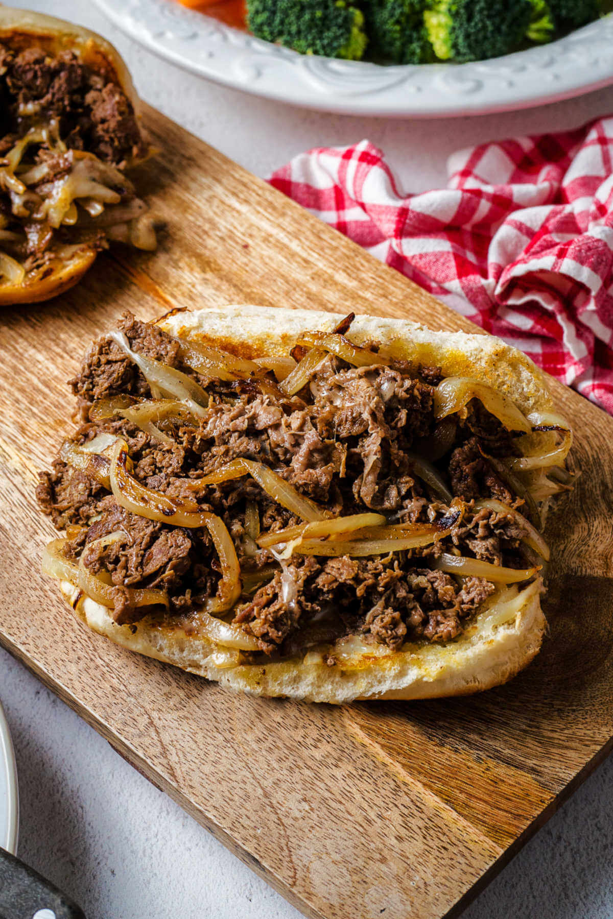 an open-face philly cheesesteak sandwich on a wooden board on a table.