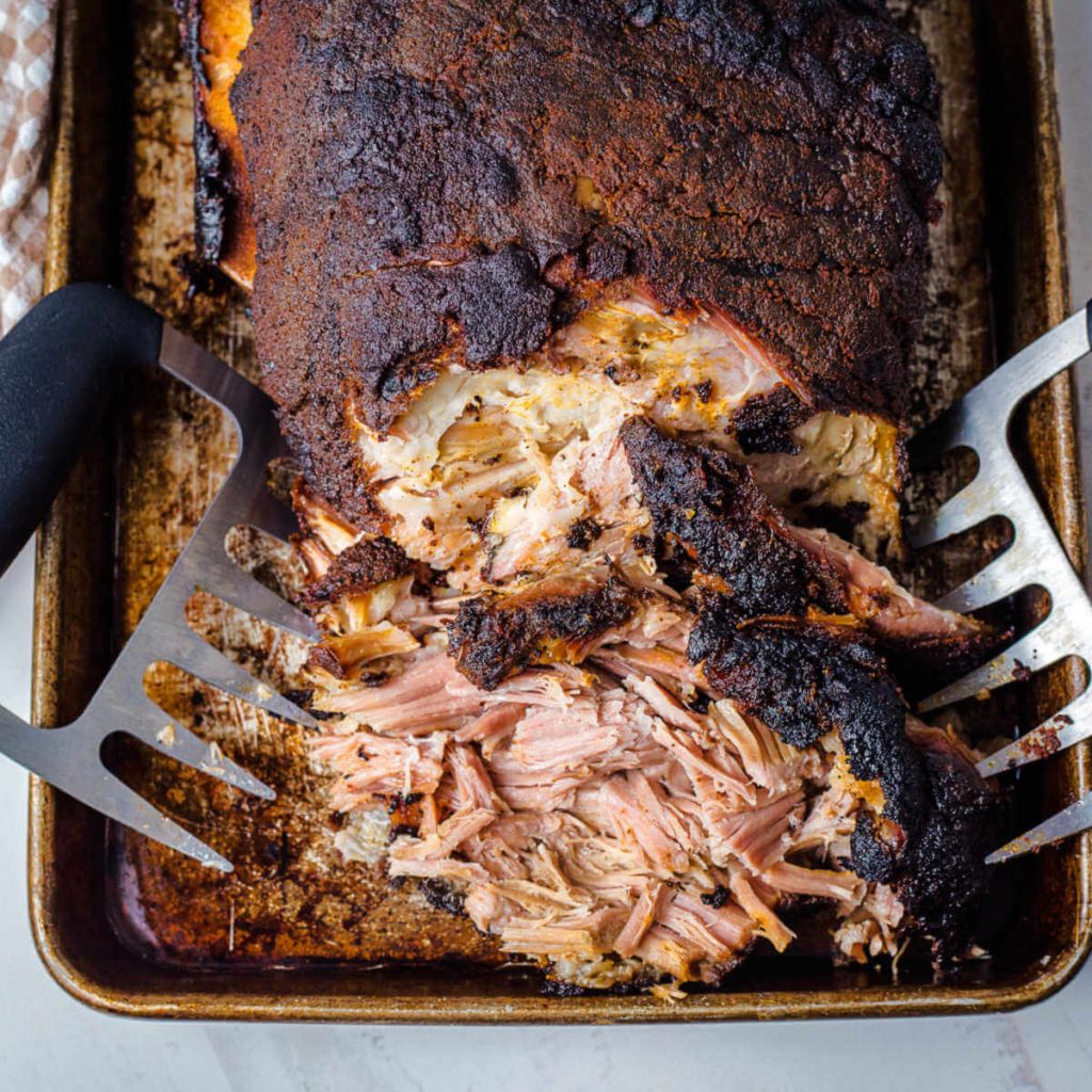 a smoked pork butt partially pulled with meat claws on a baking sheet.