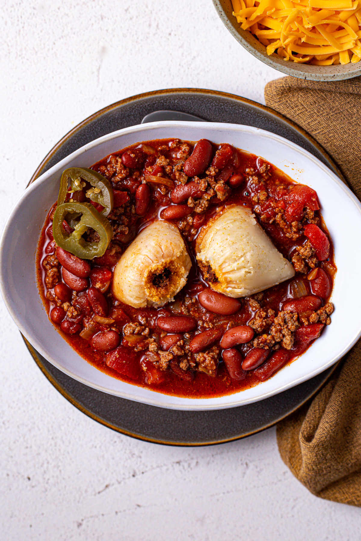A full house (hot tamales in a bowl of chili) garnished with jalapeno slices on a plate.