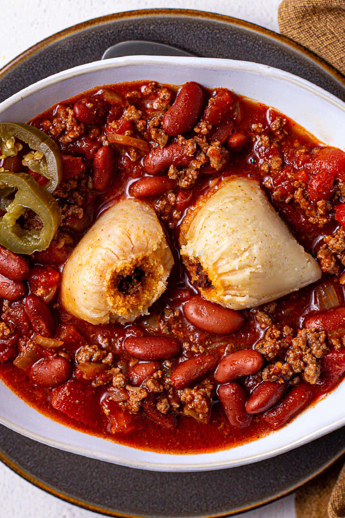 A full house (southern style hot tamales in a bowl of chili) garnished with jalapeno slices on a plate.