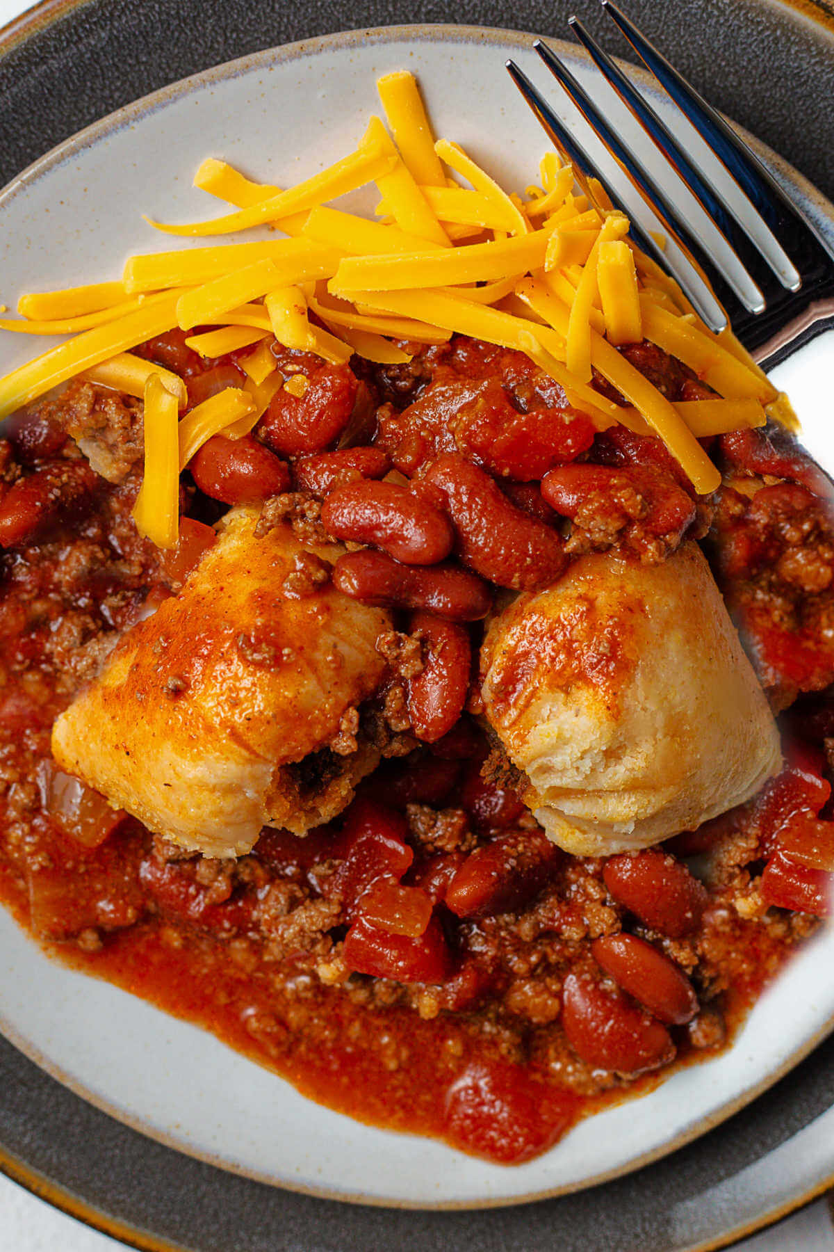 southern style hot tamales on a plate smothered with chili and cheese.