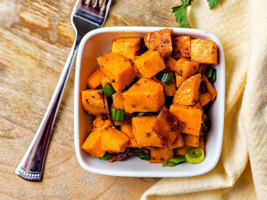 a serving of sweet potato salad in a small white bowl on a table.