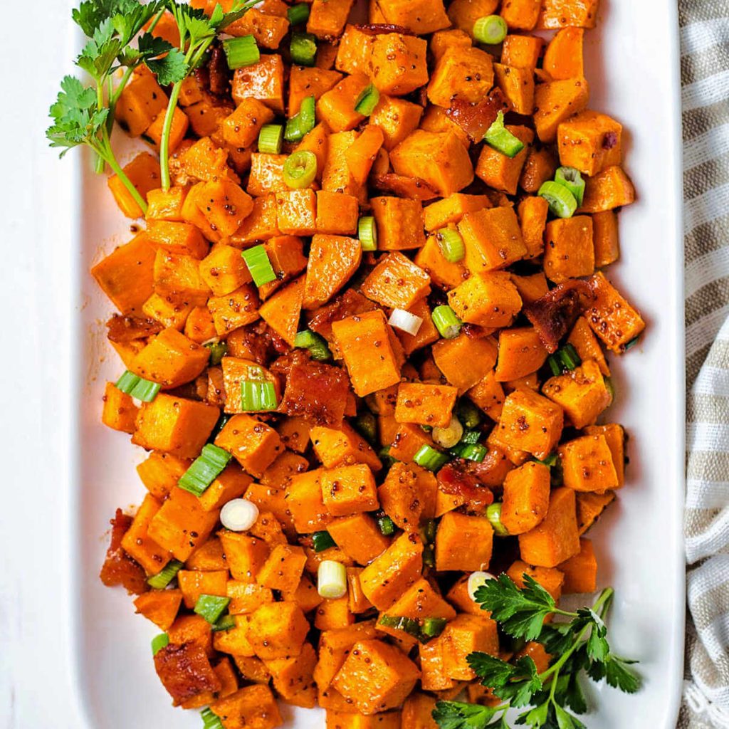 a platter of sweet potato salad garnished with fresh parsley sitting on a table with a linen napkin.