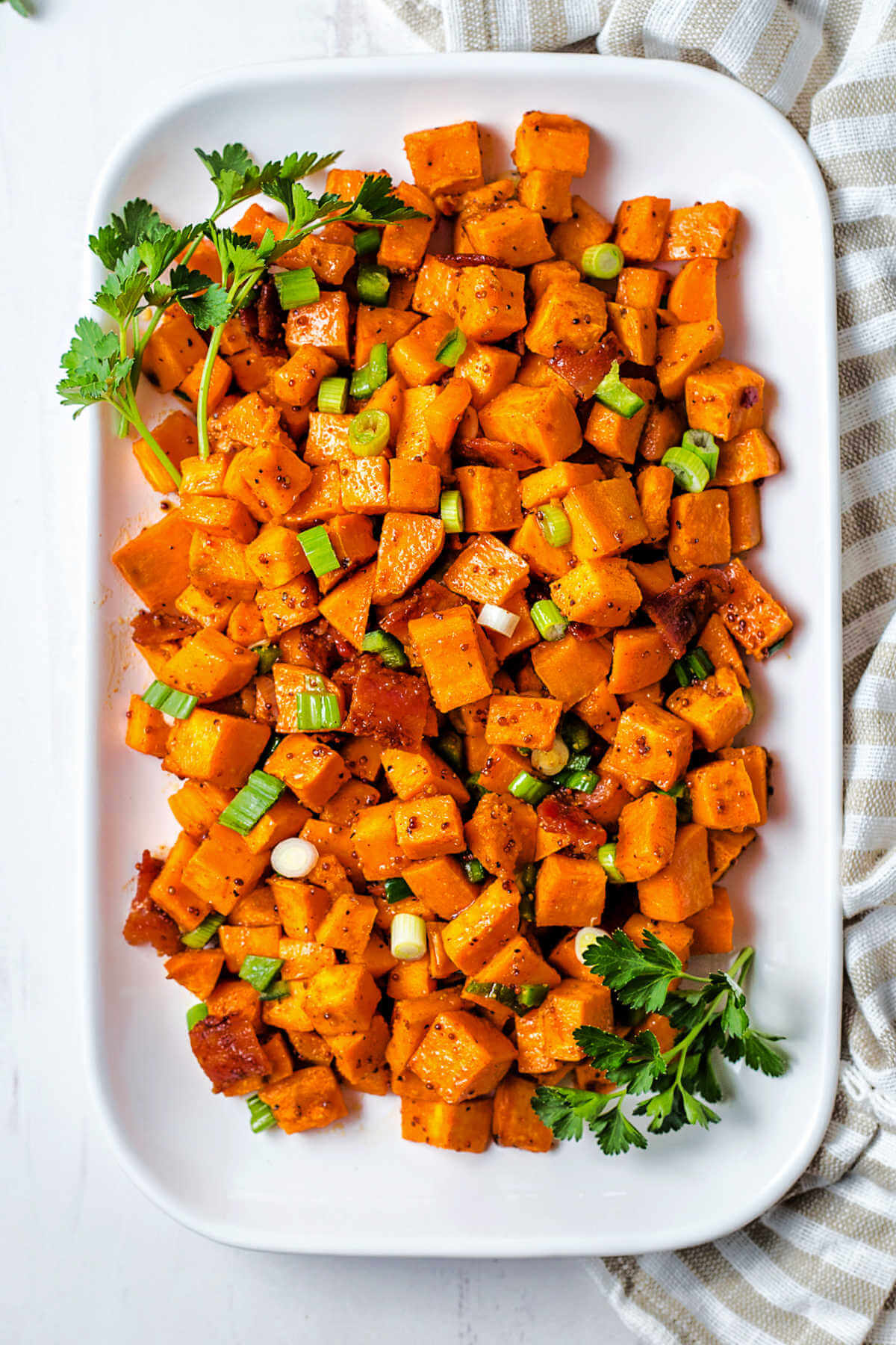 a platter of sweet potato salad garnished with fresh parsley sitting on a table with a linen napkin.