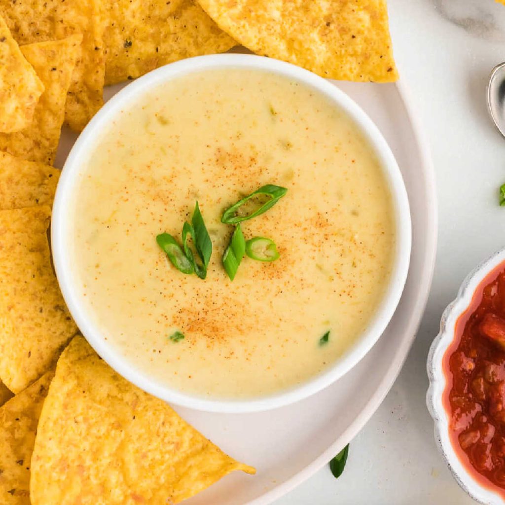 white queso dip and chips on a platter on a table.