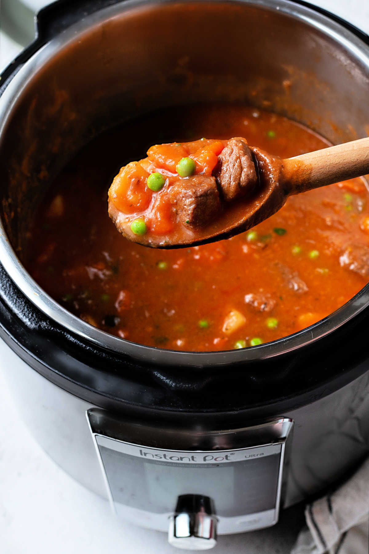 a wooden spoon lifting out a serving of instant pot beef stew from a pot.
