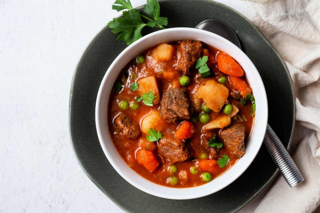 instant pot beef stew in a white bowl on a green plate garnished with fresh parsley.