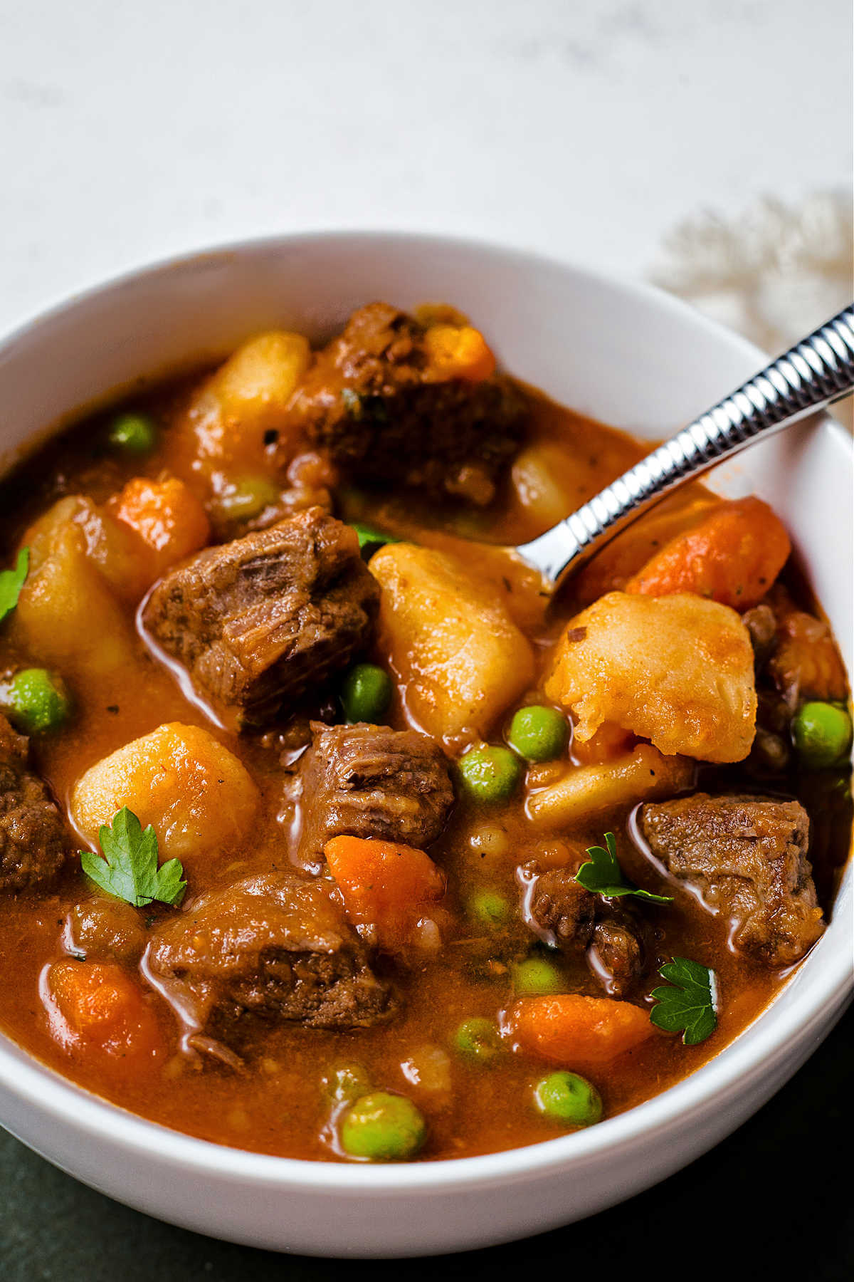 a serving of beef stew in a white bowl with a serving spoon.