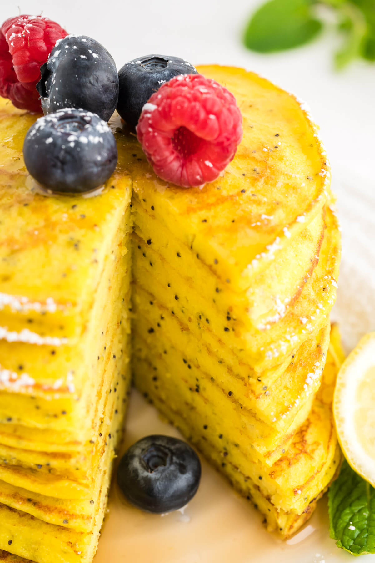 a stack of lemon ricotta pancakes on a plate with a bite missing, garnished with fresh berries sitting on a table with more berries and maple syrup.