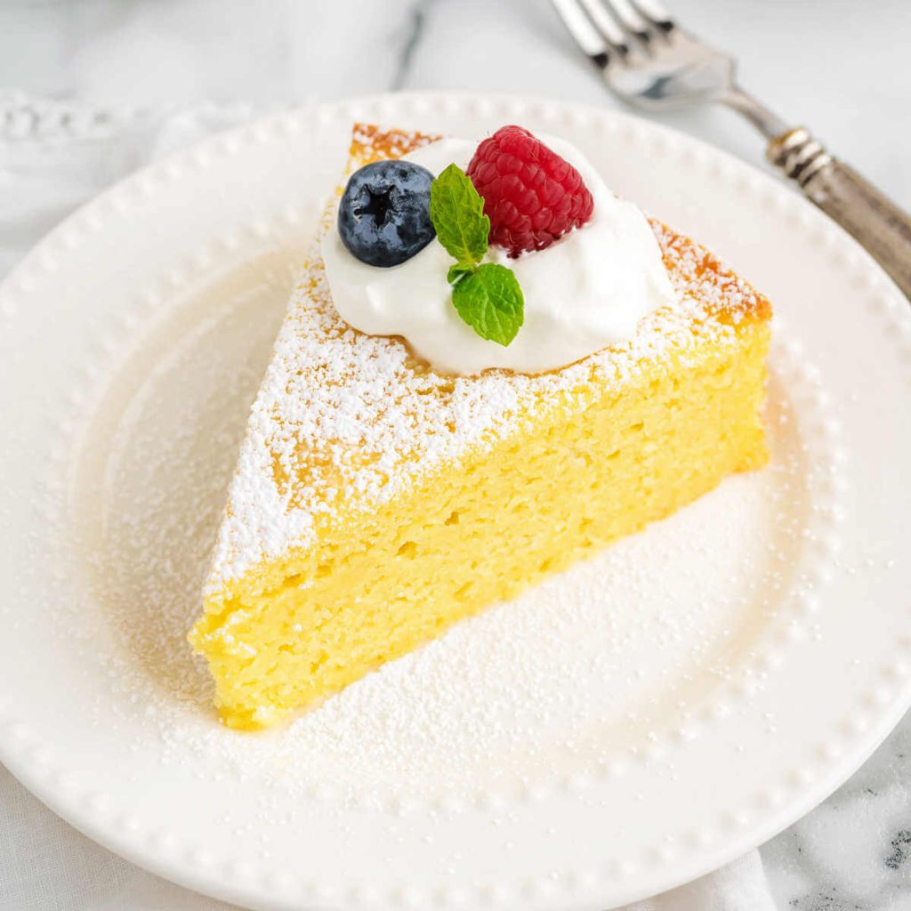 lemon ricotta cake garnished with whipped cream and berries on a plate.