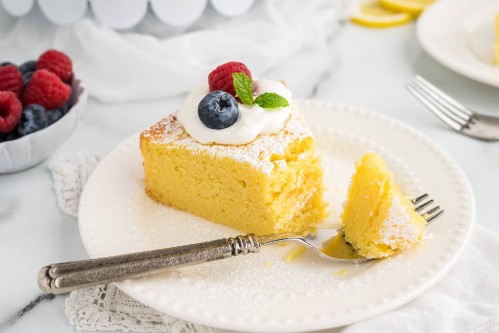 lemon ricotta cake garnished with whipped cream and berries on a plate with a fork and a bite missing.
