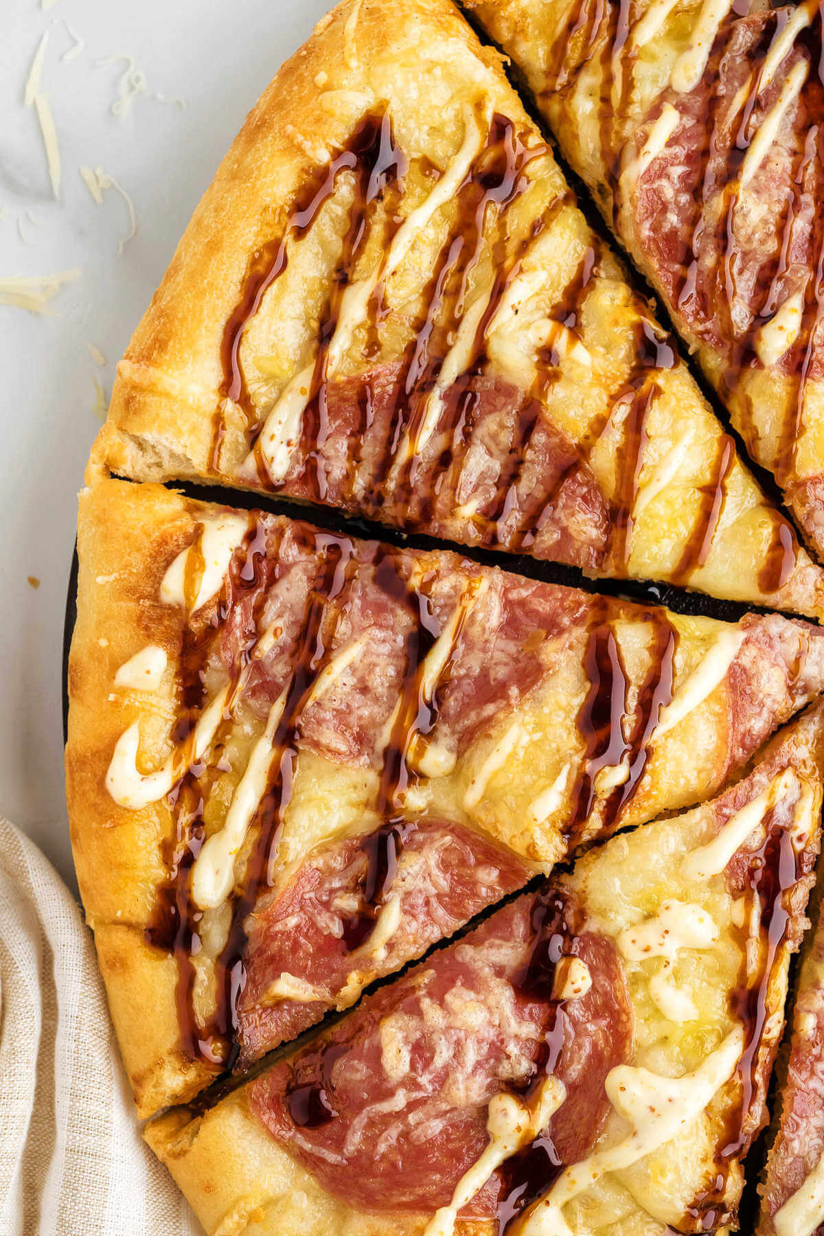 close up shot of a salami pizza cut into slices drizzled with balsamic vinegar and garlic aioli.