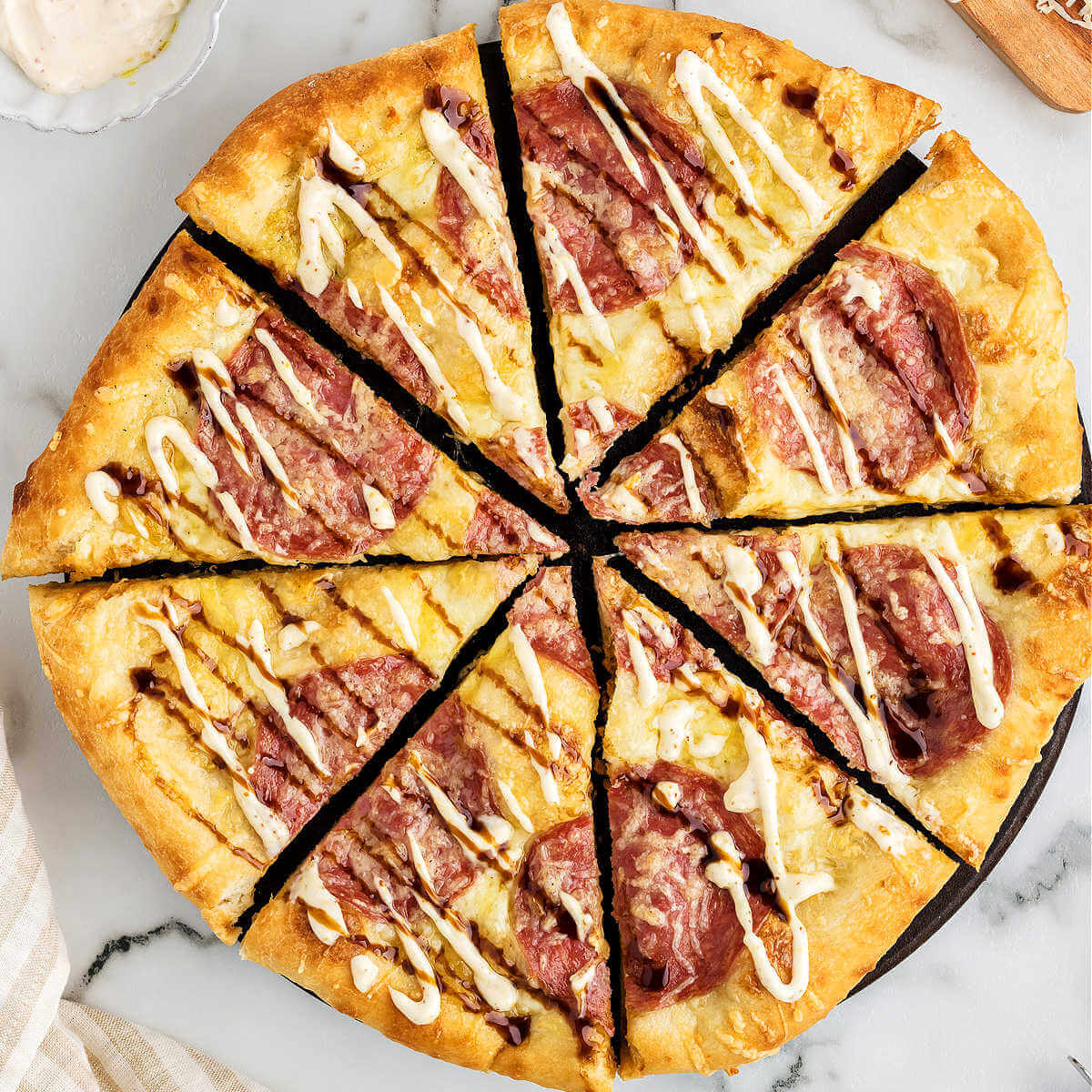 a salami pizza cut into slices on a pizza stone.