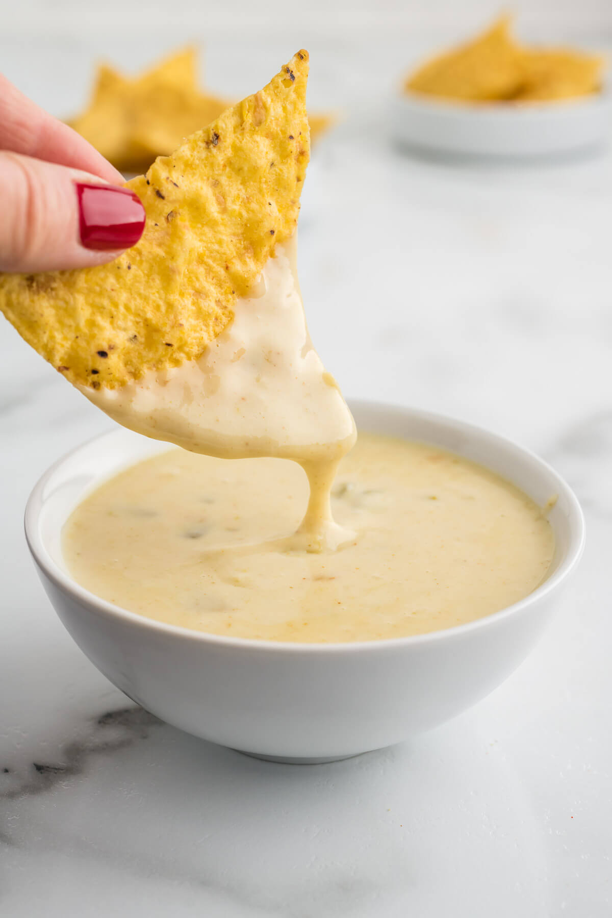 dipping a tortilla chip into a bowl of white queso dip.