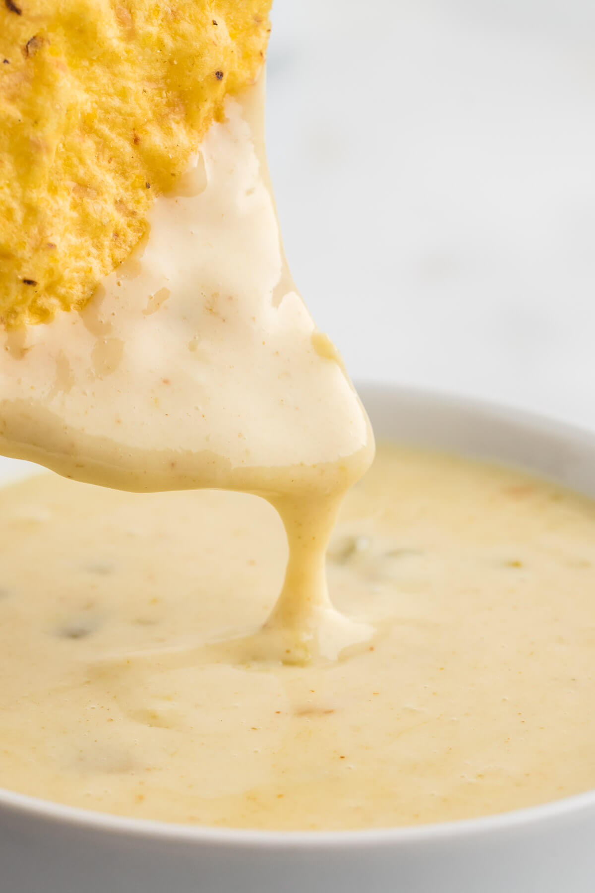 close up image of white queso dip dripping off a tortilla chip.