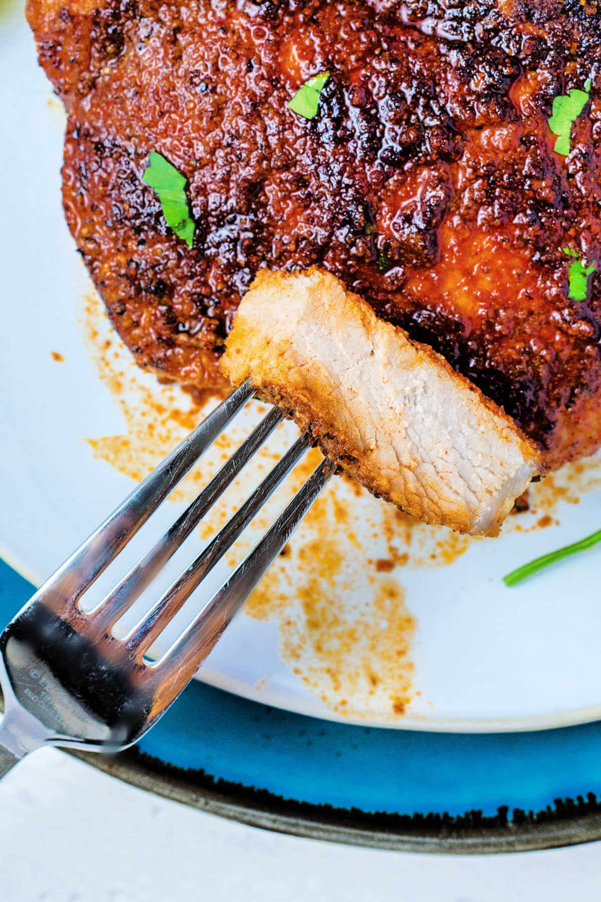 a slice of pork chop on a fork resting on a plate.