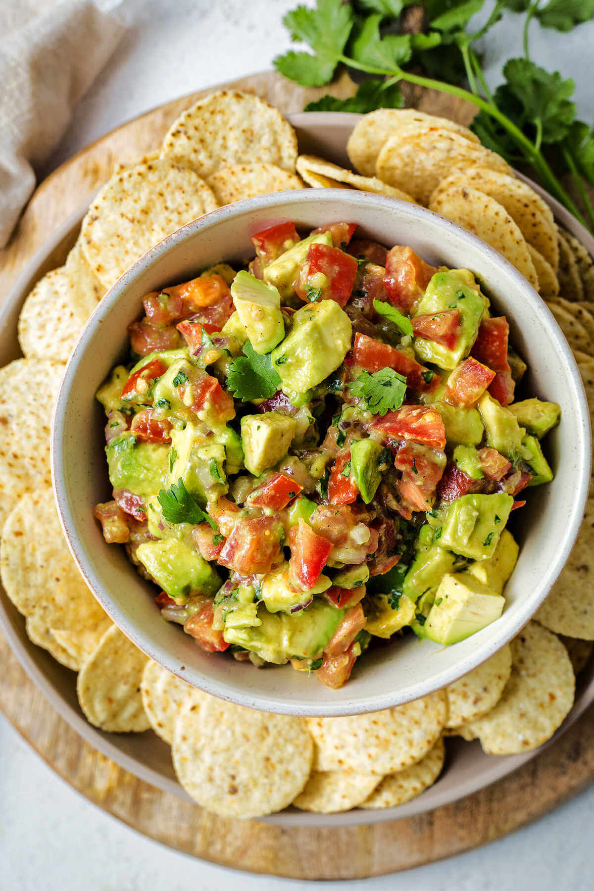 a bowl of avocado salsa on a tray with tortilla chips on a table.
