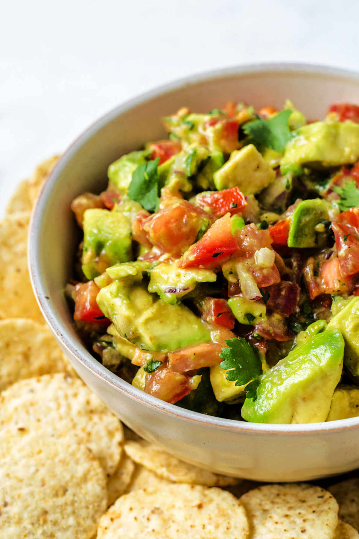 close up image of avocado salsa in a bowl on a platter surrounded by tortilla chips on a table.