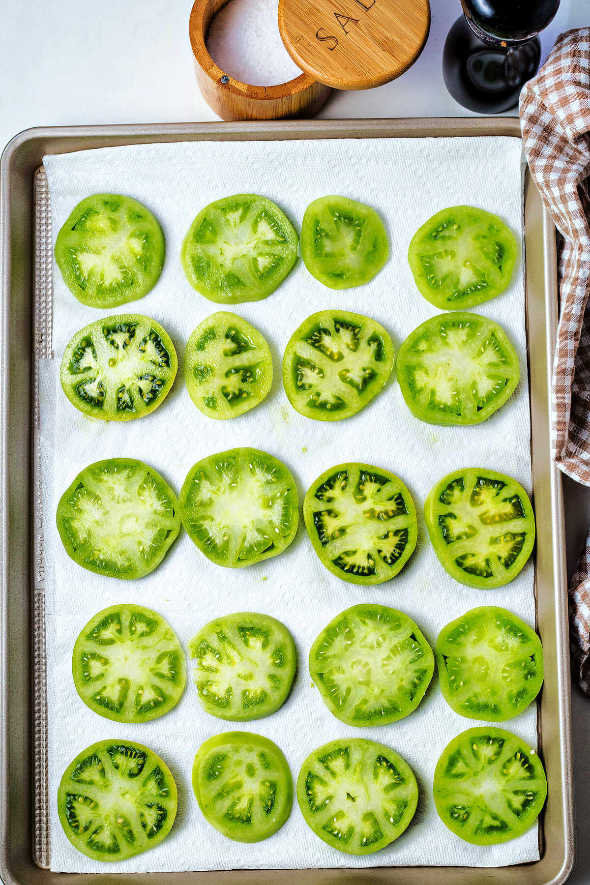 salted green tomato slices on a paper towel lined baking sheet.