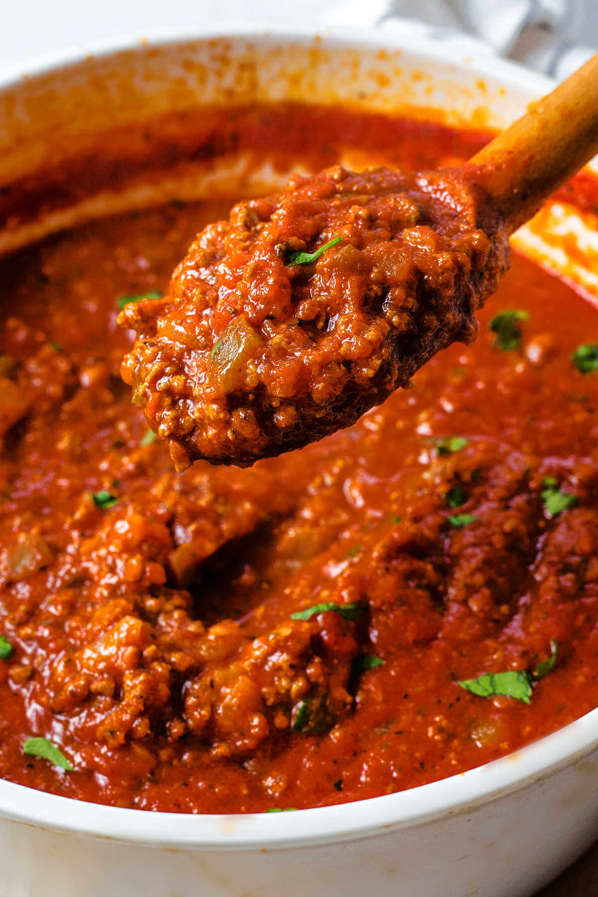 a wooden spoon lifting out a scoopful of Italian meat sauce from a pot.