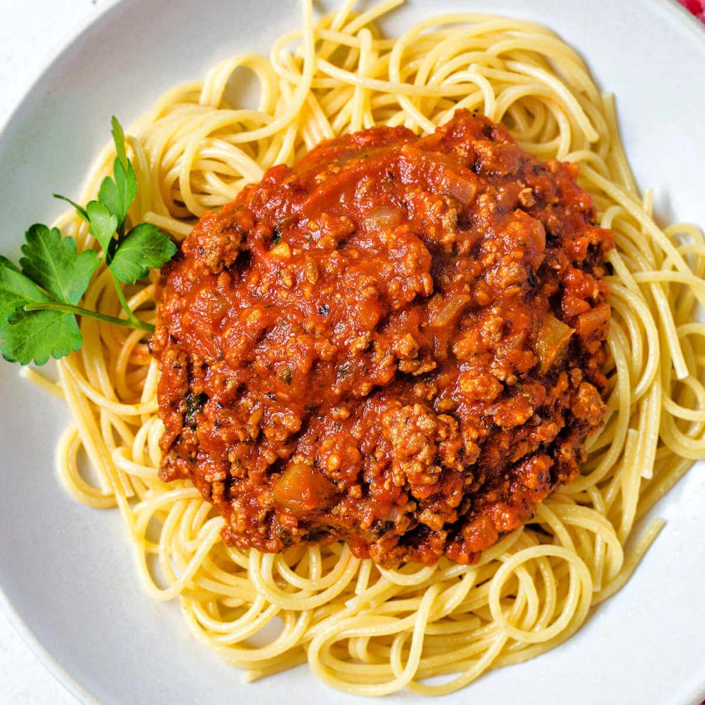 Italian meat sauce on a bed of spaghetti noodles in a white bowl.