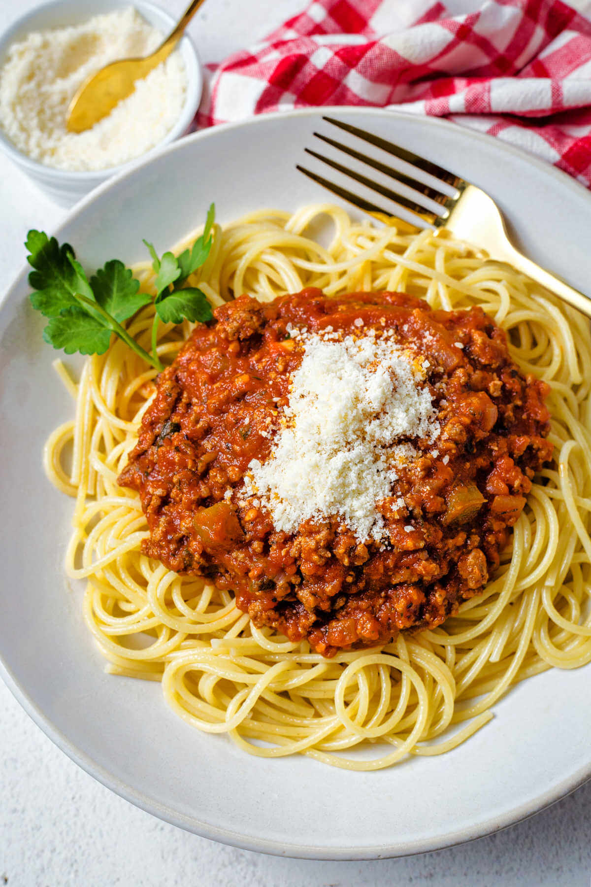 Italian meat sauce topped with parmesan cheese on a bed of spaghetti noodles in a white bowl.