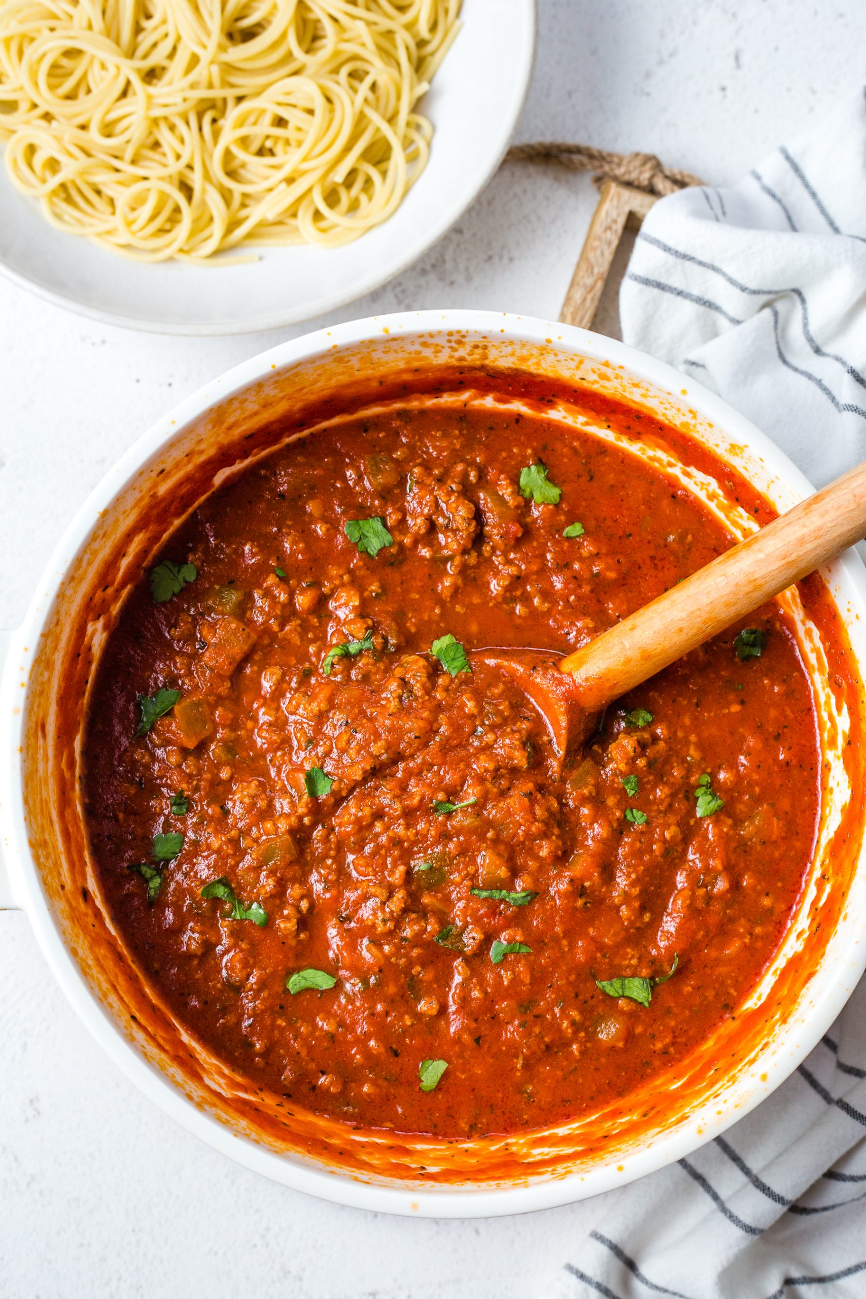 Italian meat sauce in a dutch oven on a table with a bowl of noodles.