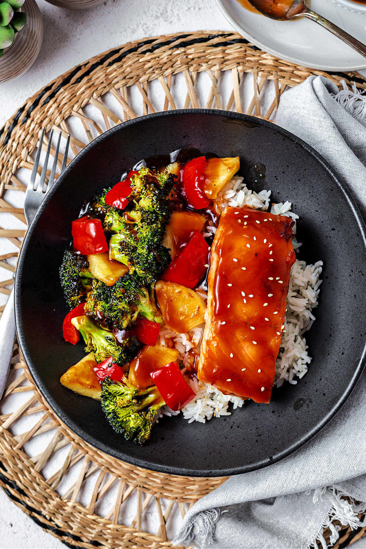 a salmon bowl with homemade teriyaki sauce drizzled over the ingredients sitting on a woven placement on a table.