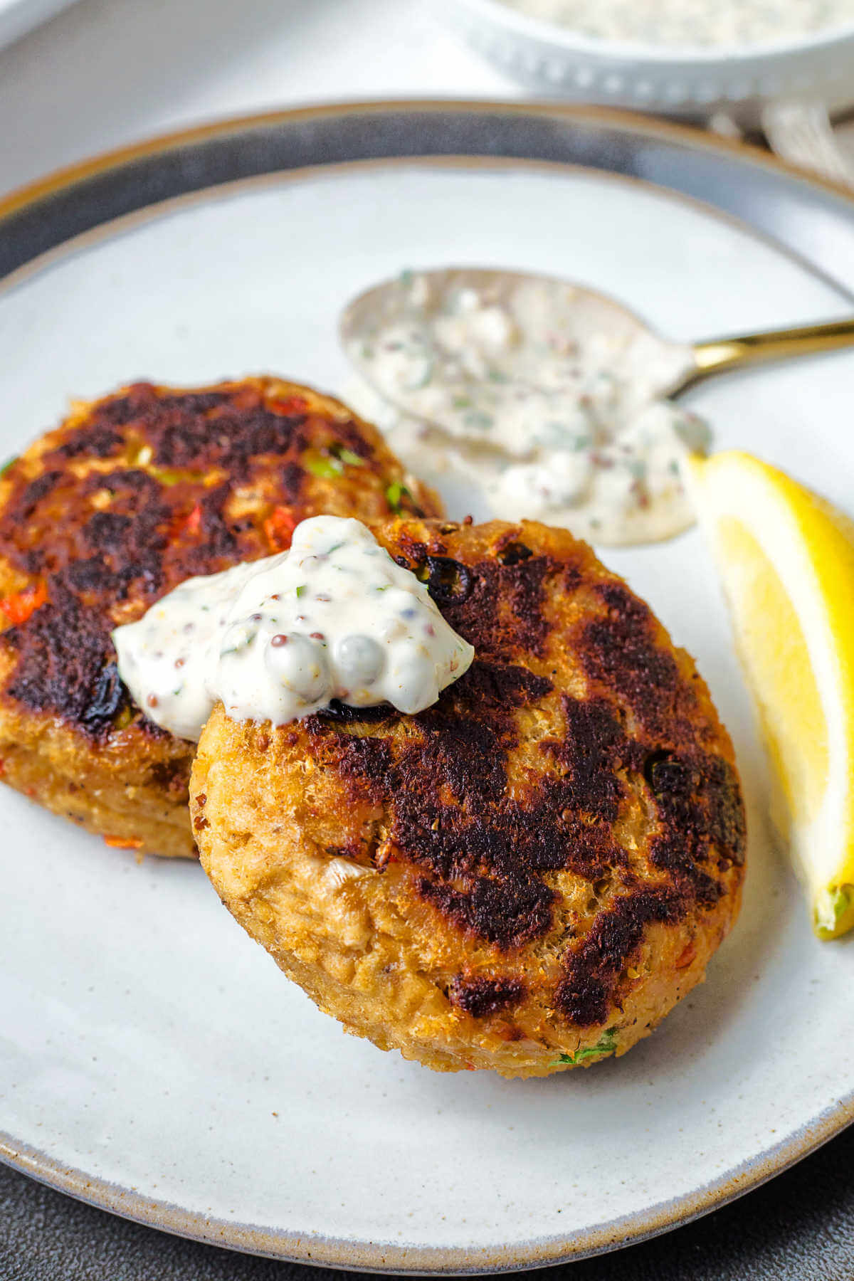 two salmon croquettes on a plate with a dollop of tartar sauce on top of the croquette.