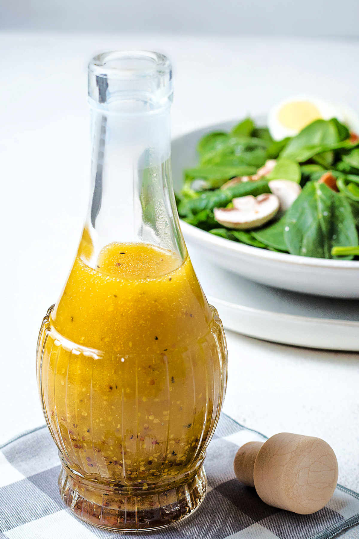 spinach salad dressing in a glass bottle with a bowl of salad in the background.