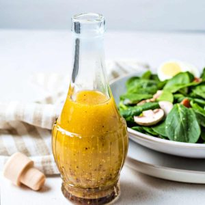 spinach salad dressing in a glass bottle with a bowl of salad in the background.