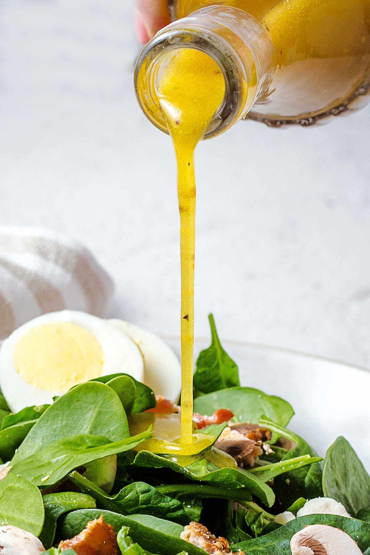 pouring spinach salad dressing onto a bowl of salad.