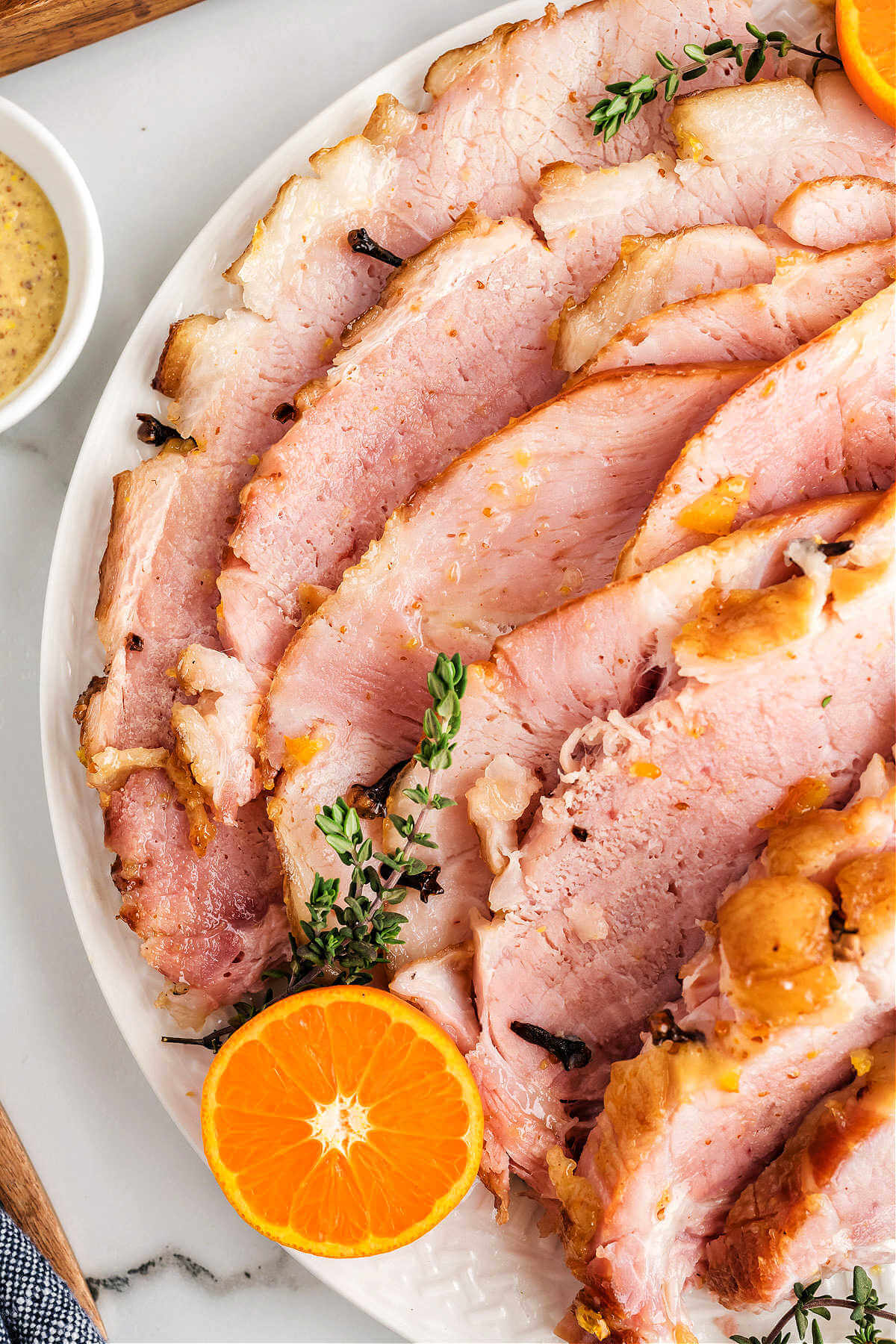 close up.image of slices of baked ham on a platter garnished with orange slices on a table.