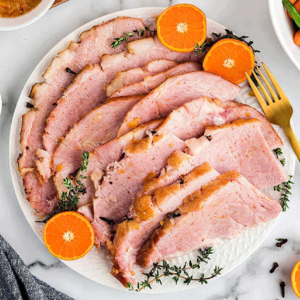 slices of baked ham on a platter garnished with orange slices on a table.