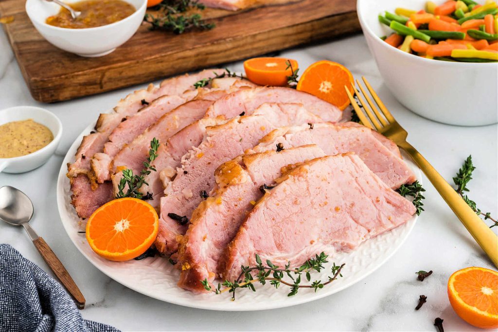slices of baked ham on a platter garnished with orange slices on a table.