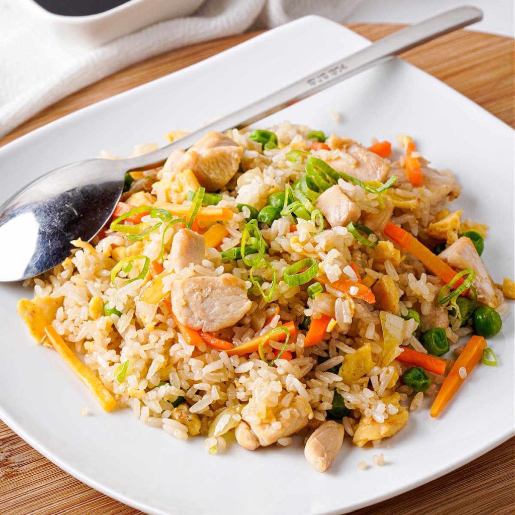 chicken fried rice on a white platter with a serving spoon to the side.