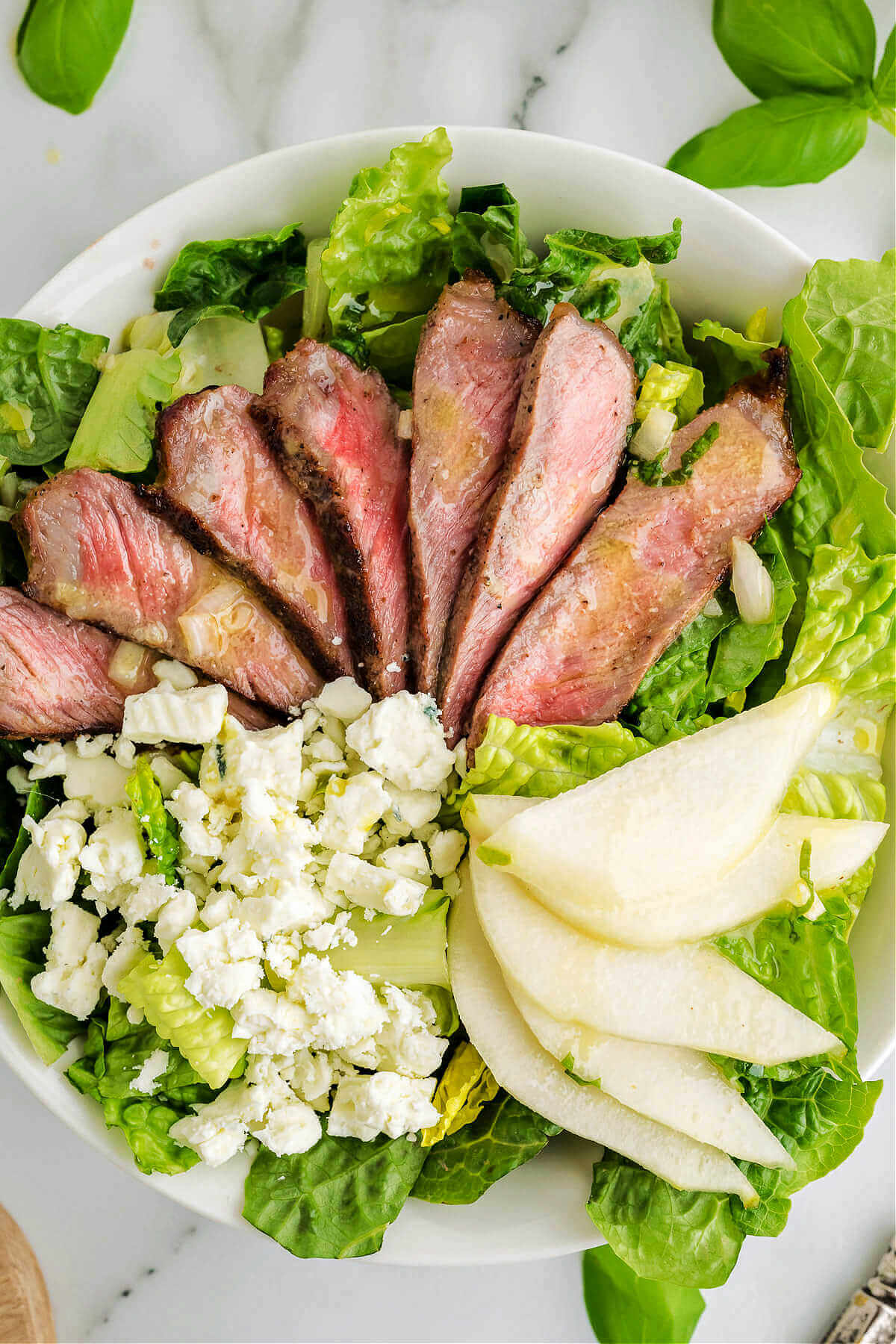 grilled steak salad with sliced pears, blue cheese, and French vinaigrette in a bowl on a table.