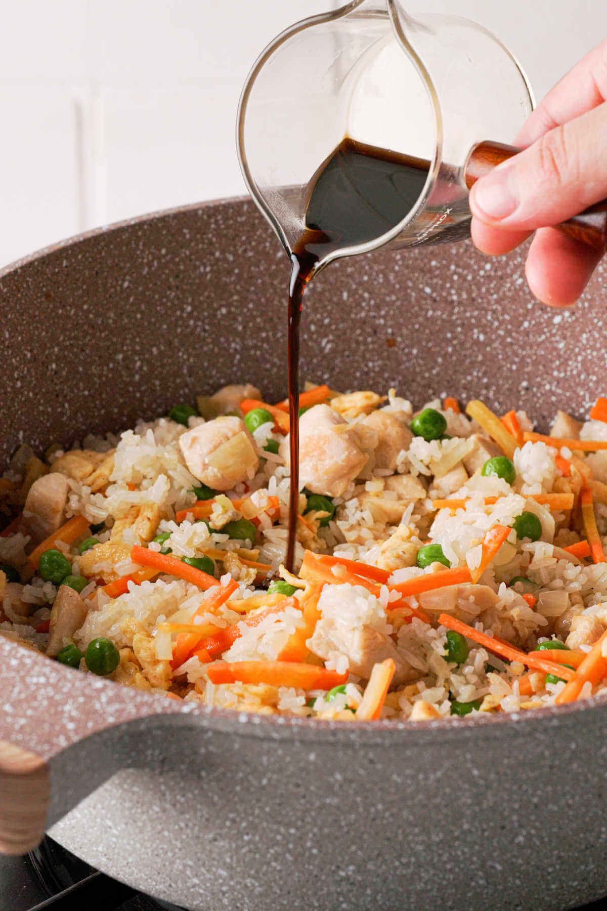 pouring soy sauce into fried rice in a wok.