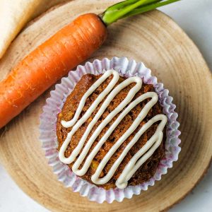 top down view of a carrot cake muffin on a wooden board with a whole carrot to the side.