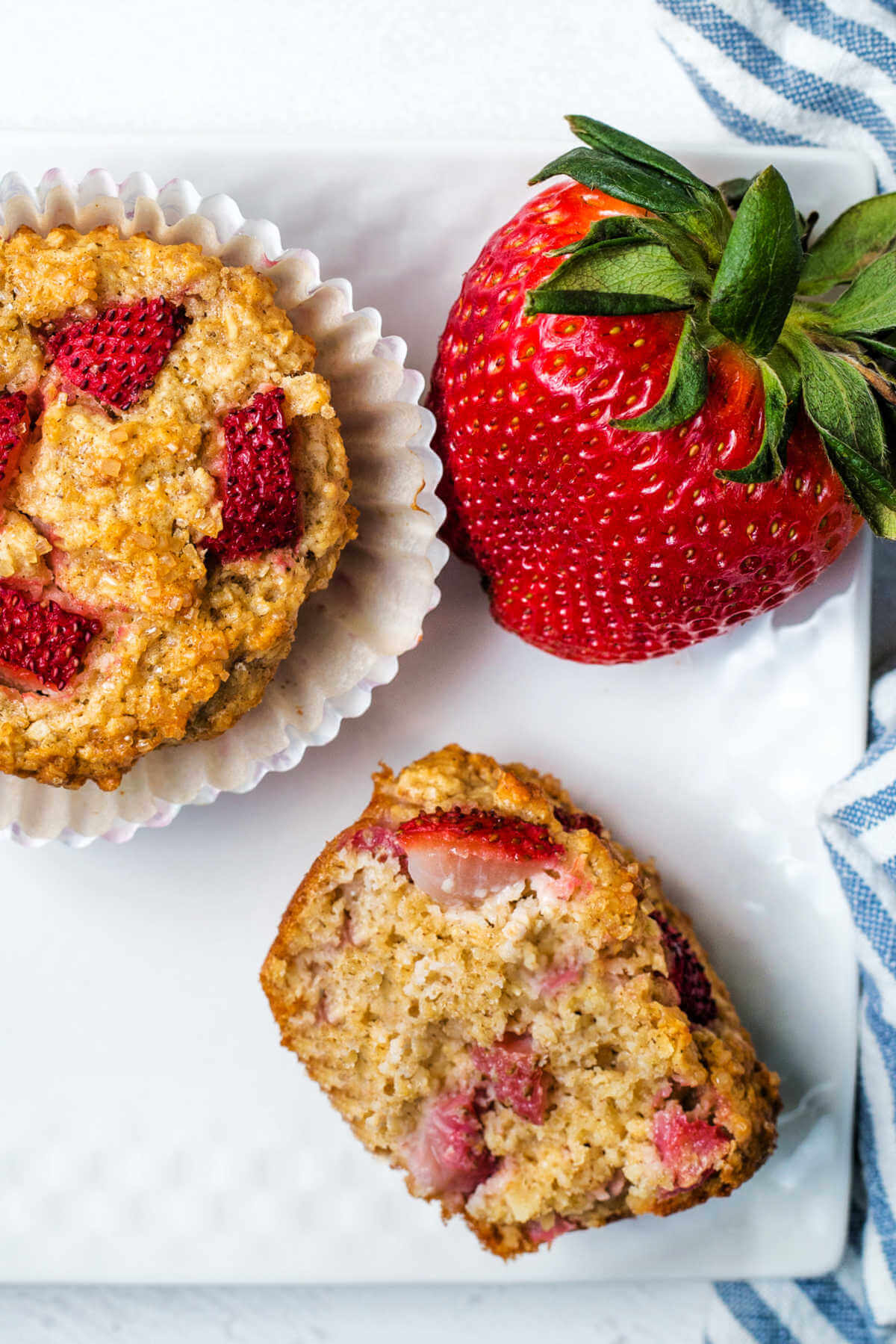 a strawberry oat muffin torn in half on a plate with a strawberry garnish.