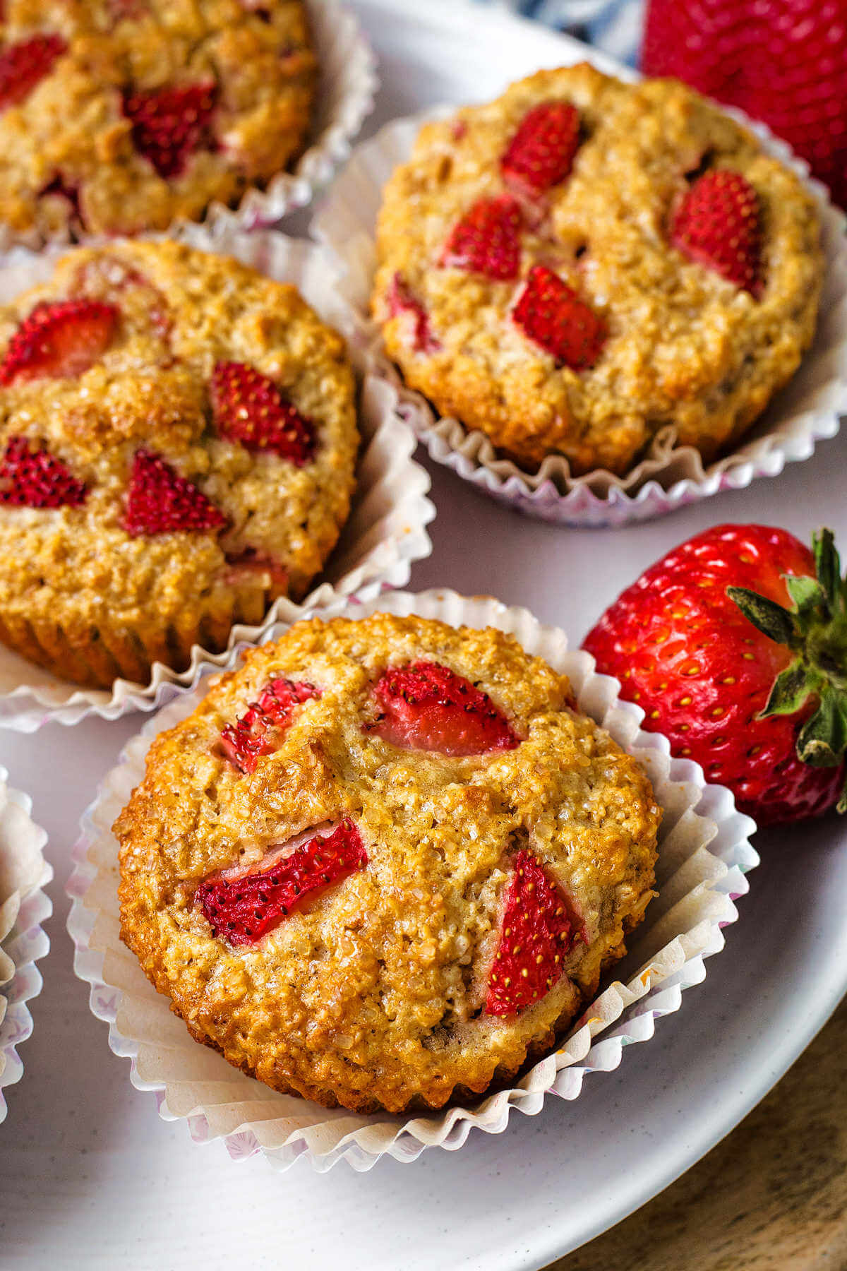 strawberry oat muffins on a white plate with strawberry to the side on a table.