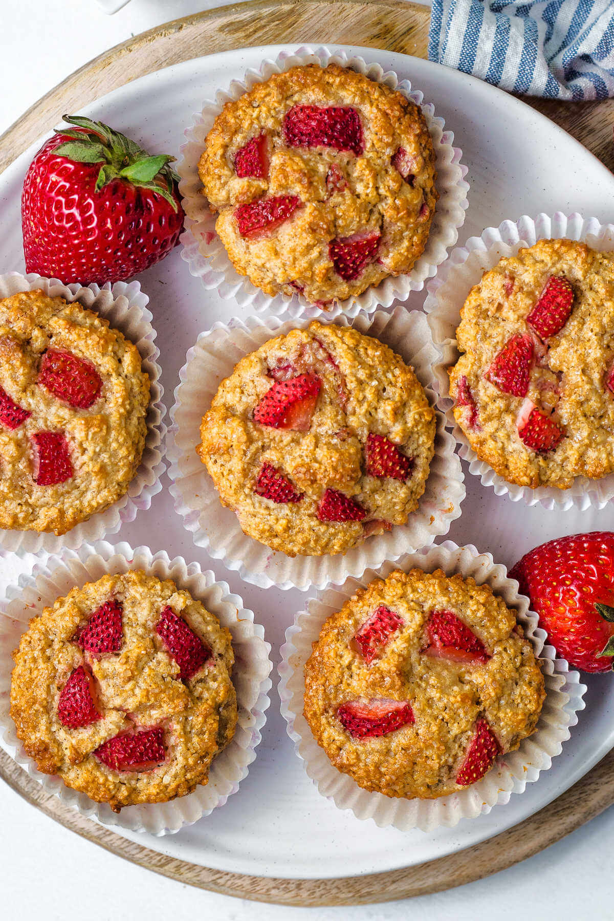 a half dozen strawberry oat muffins on a white plate with strawberry to the side on a table.