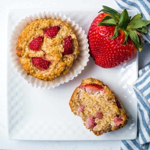 strawberry oat muffins on a serving plate with a whole strawberry to the side.