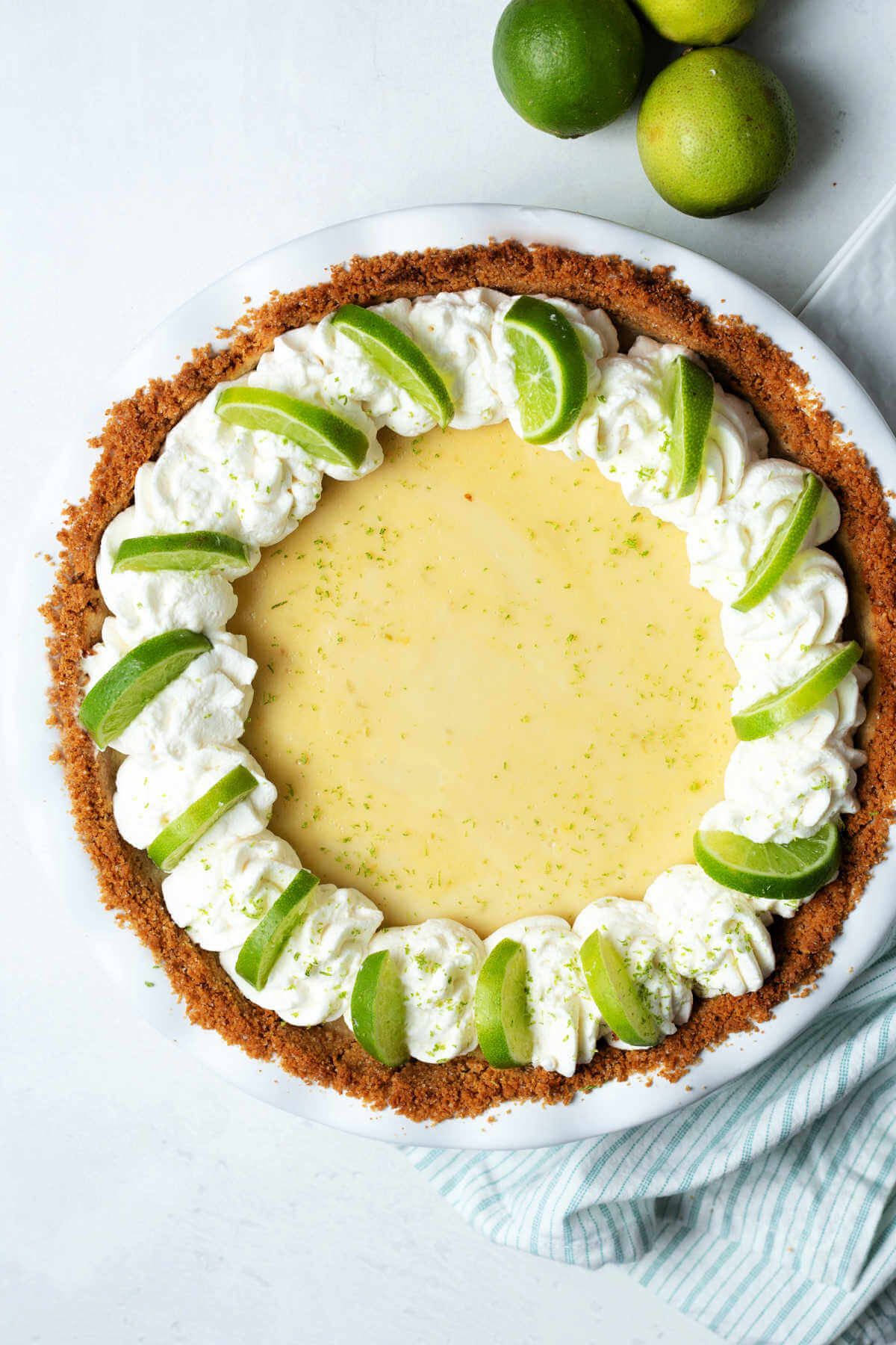 a whole key lime pie garnished with fresh whipped cream and lime slices on a table with limes.