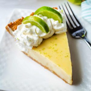 a slice of key lime pie garnished with fresh lime slices and lime zest on a plate with a fork.
