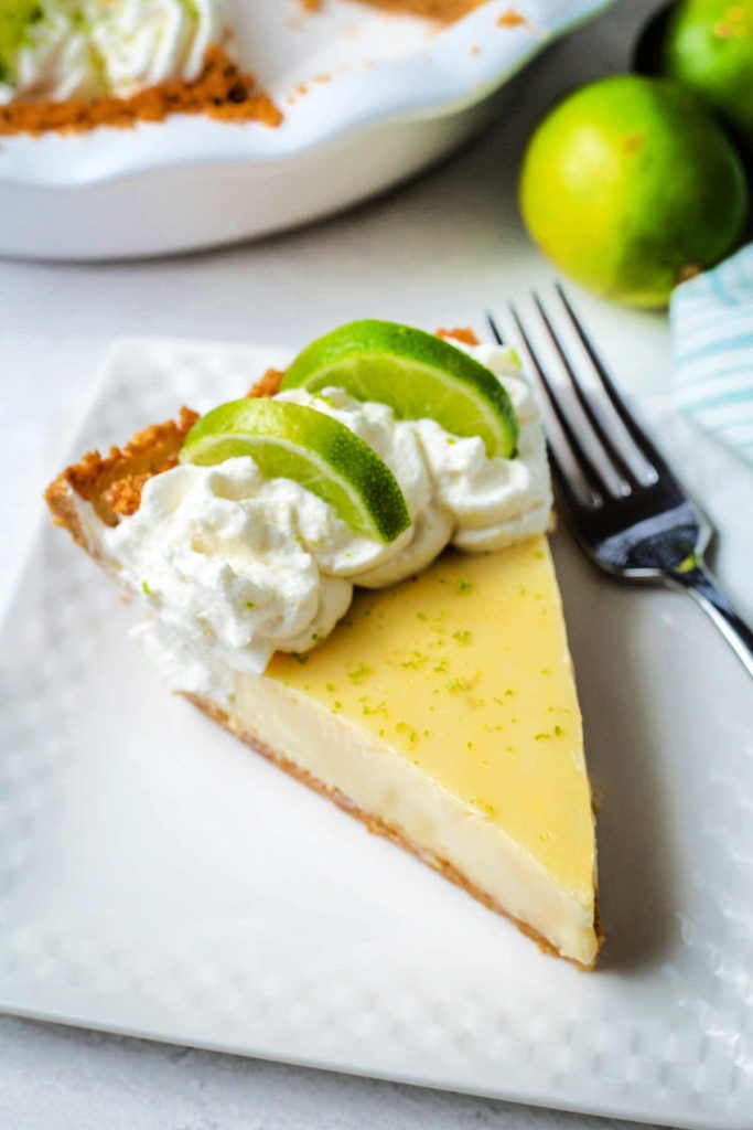 a slice of key lime pie garnished with fresh lime slices and lime zest on a plate with a fork.