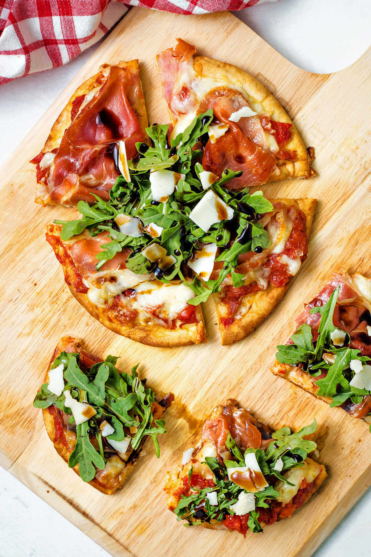 pita bread pizza with prosciutto, arugula, and balsamic vinegar drizzled on top cut into quarters on a pizza peel.