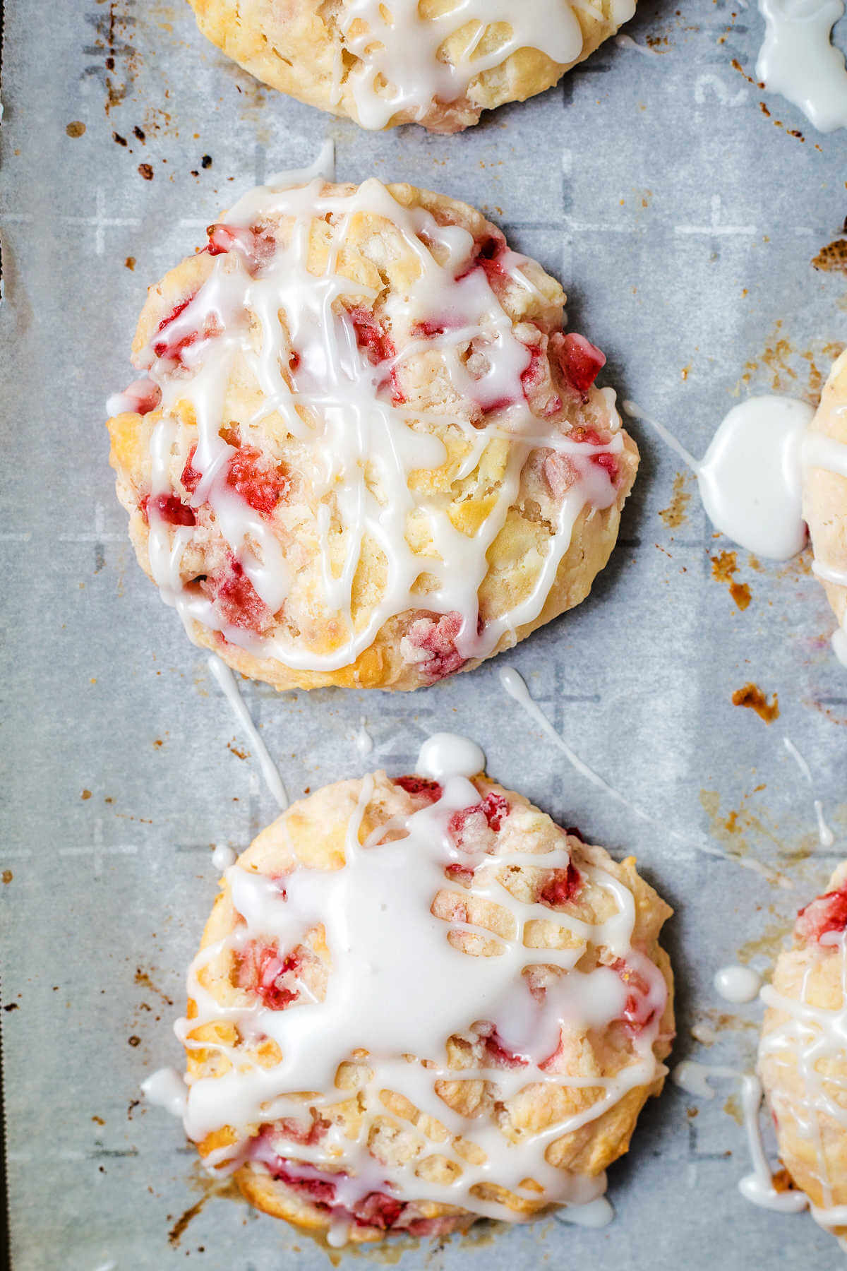 strawberry biscuits drizzled with powdered sugar glaze on a parchment paper lined baking sheet.
